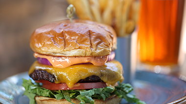 cheddar burger with fries and beer in background